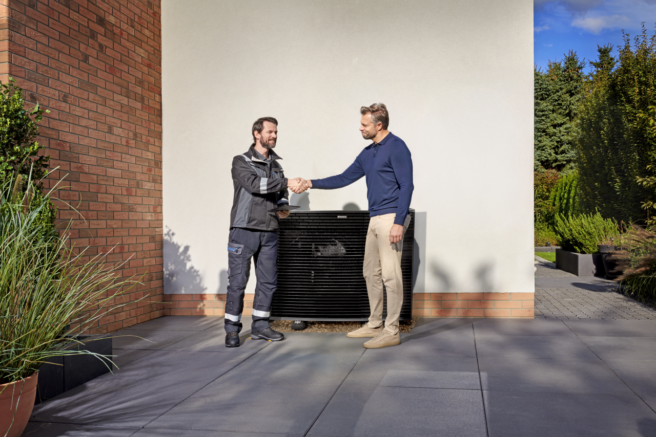 Uzstādītājs paspiež klienta roku blakus Daikin Altherma āra ierīcei